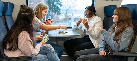 Vier Schülerinnen sitzen im Zug und spielen UNO