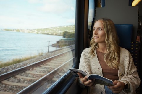 Woman sitting on the train with a brochure in her hand and looking out of the window.