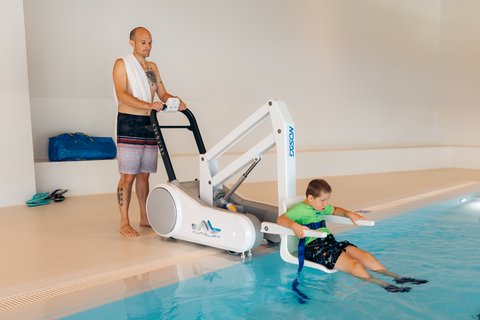 Swimming pool lift in the Aua Grava indoor pool at wellnessHostel 3000 in Laax A man operates the pool lift in the Aua Grava indoor pool at wellnessHostel 3000 in Laax. His son sits in the front seat and is lowered into the children's pool.
