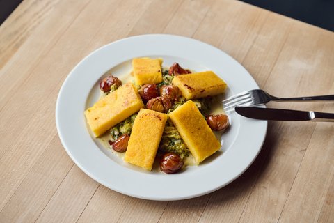 Teller mit Polentaschnitten mit Rahmwirsing und glasierten Marroni. Am Teller angelehnt, Messer und Gabel.