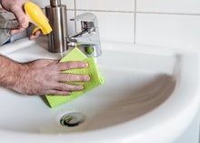 Ein Mann reinigt ein Waschbecken mit Lappen und Putzmittel.