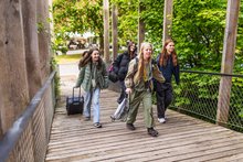 Mädchen laufen mit Gepäck über eine Holzbrücke und freuen sich. 