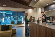 Zwei Gäste, ein Mann und eine Frau, stehen an Tresen des Bistro 4000 im wellnessHostel in Saas-Fee. Ein Mitarbeiter zapft ein Bier.