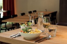 Auf einem Tisch im Restaurant 3a in der Jugendherberge Interlaken steht ein Hauptgang, ein schöner Salat mit Croutons, eine Wasserkaraffe, ein Wasserglas und ein Glas Apfelsaft