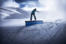 A snowboarder does a trick, riding a frontside over a rail