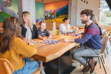 Eine Familie sitzt im Restaurant der Jugendherberge Laax wellnesshostel 3000am Tisch und spielt. Die Familie besteht aus zwei Mädchen, Mutter und Vater.