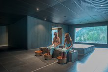 Ein Mann und eine Frau sitzen in einem zentralen Bereich des Aqua Allalin, im wellnessHostel 4000 und Baden die Füsse in Holzeimern.
