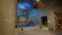 Fire bath at Aua Grava wellnessHostel3000 in Laax. The walls are made of granite, the ceiling reflects coloured light from the ceiling lamp and the water.