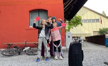 Eine Mutter mit drei Kindern steht vor der Jugendherberge Baden. Zwei Kinder haben Ping-Pong-Schläger in der Hand. Vor ihnen steht ein Koffer.