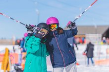 Zwei Kinder im Jubiläums-Skilager der Schweizer Jugendherbergen sind auf der Piste. Sie tragen Skikleidung, Helme und Skistöcke.