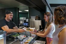 Mitarbeiter überreicht das Essen einem Gast. 