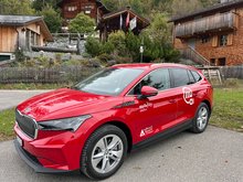 A Mobility rental electric car with the logo of wellnessHostel3000 Laax stands in front of buildings in Graubünden
